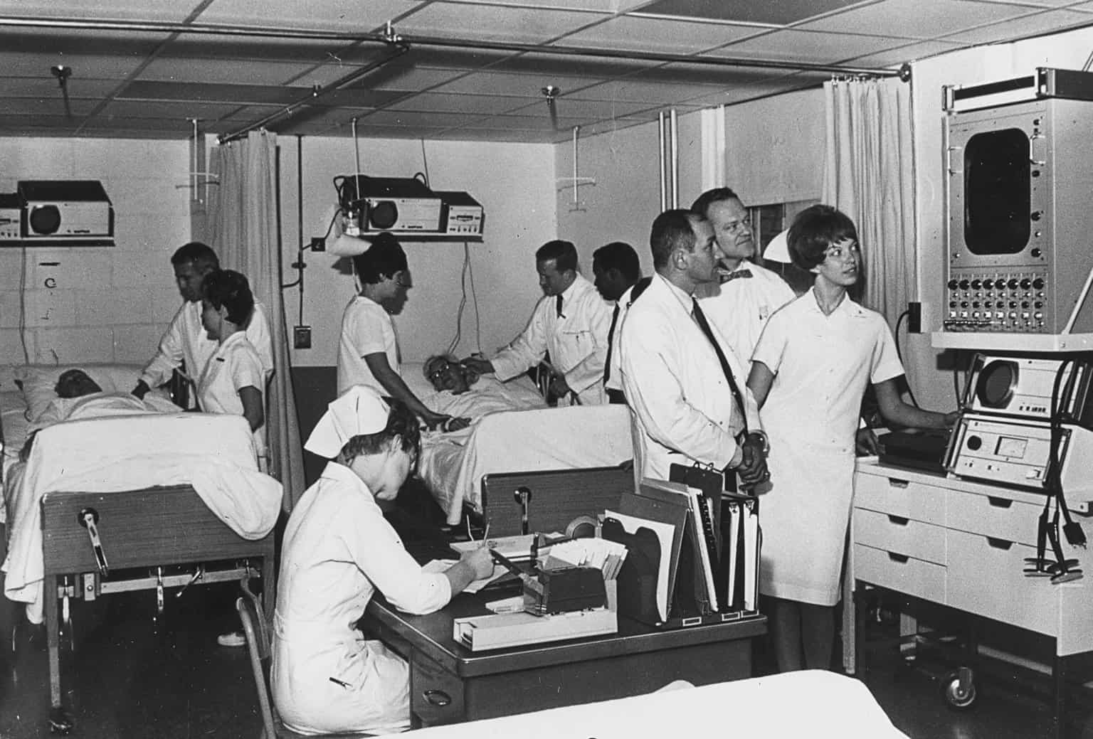 A black and white photo from the mid-20th century of a hospital room with multiple nurses and doctors working
