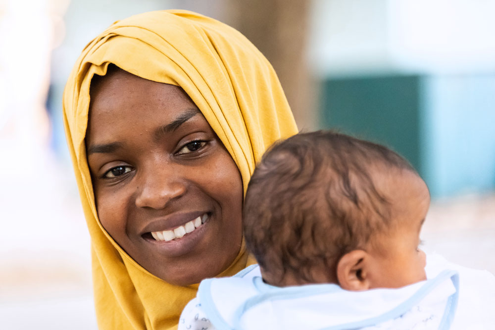 East African woman with hijab smiling while holding infant