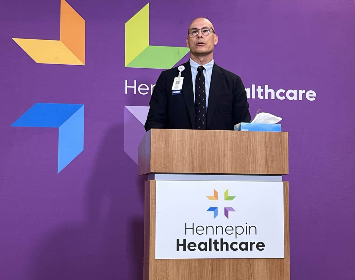 dr. thomas wyatt, chair of emergency medicine, speaking at podium in front of hennepin healthcare logo and background