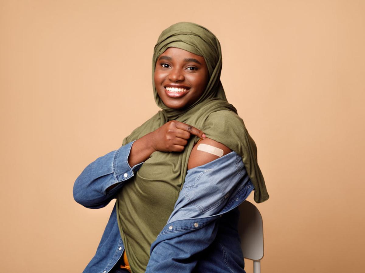 East African woman with hijab shows off her arm and bandage after getting vaccinated