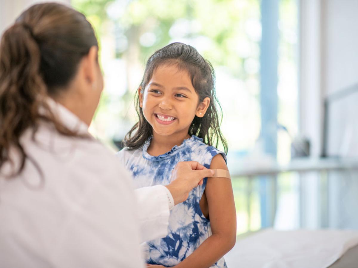 School age Latina girl smiling while getting a vaccinated by doctor