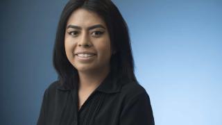female in black shirt smiling with a blue background