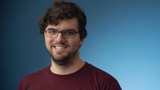 Male smiling with glasses wearing a burgundy shirt