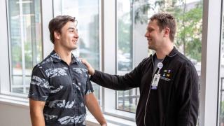 male employee with hand on shoulder of another male smiling.