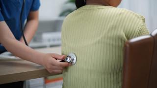 nurse holding a stethoscope on the back of a patient