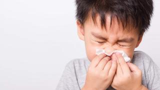 young boy blowing his nose in a wipe with eyes closed