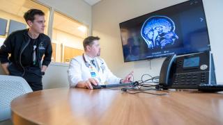Two medical professionals reviewing a brain scan displayed on a monitor in a clinical conference room.
