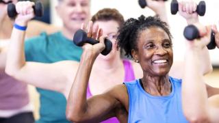 group fitness class older woman at front of class lifting weights
