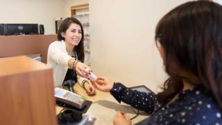 Pharmacist smiling and handing a prescription bottle to a customer at the pharmacy counter.