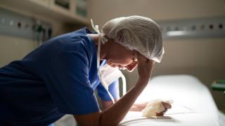provider exhausted leaning over bed with hand on her forehead wearing scrubs and a hair net