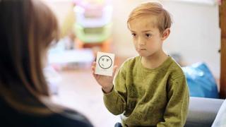 young boy holding card that says sorry with provider looking at him