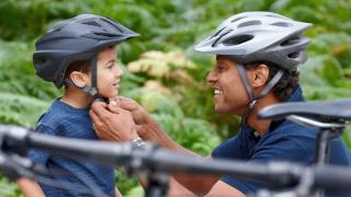 Father in a bike helmet putting helmet on his young son