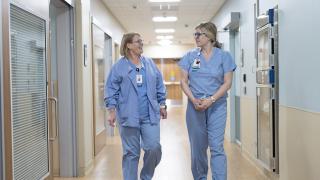 two providers wearing scrubs walking and talking in the emergency room hallway