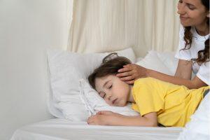 A young child lies on their side in bed during a recovery position, while an adult gently supports their head, indicating post-seizure care.