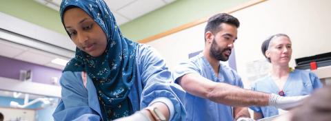 Healthcare professionals in scrubs and gloves working together in a clinical setting, focused on patient care.