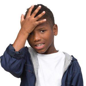 A young boy holds his forehead with a pained expression, indicating he may have bumped his head.