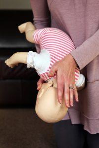 An adult demonstrates how to help a choking infant by holding the baby face-down along their forearm and delivering firm back blows between the shoulder blades.