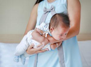 An adult holds an infant face-down along their forearm in a recovery position, supporting the baby’s head and body after a possible seizure episode.
