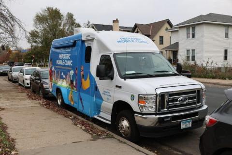 A colorful Pediatric Mobile Clinic van from Hennepin Healthcare is parked on a residential street, providing healthcare access to children in the community.