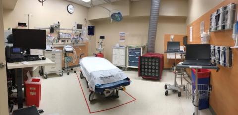 A trauma response room at Hennepin Healthcare, featuring a central patient bed surrounded by advanced medical equipment, monitors, ventilators, carts, and computers, all organized for emergency care.