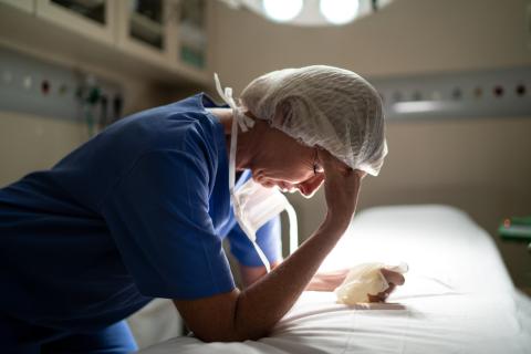 provider exhausted leaning over bed with hand on her forehead wearing scrubs and a hair net