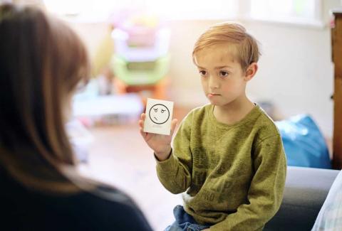 young boy holding card that says sorry with provider looking at him