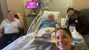 Rick Smith in hospital bed with family members at his side