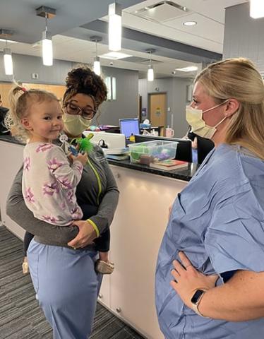 kelsie being held by nurse by nurses station in hyperbaric chamber hallway, dog attack, girl suffers ear amputation, successful hyperbaric treatment, kenzie riemenschneider, facial lacerations from dog attack