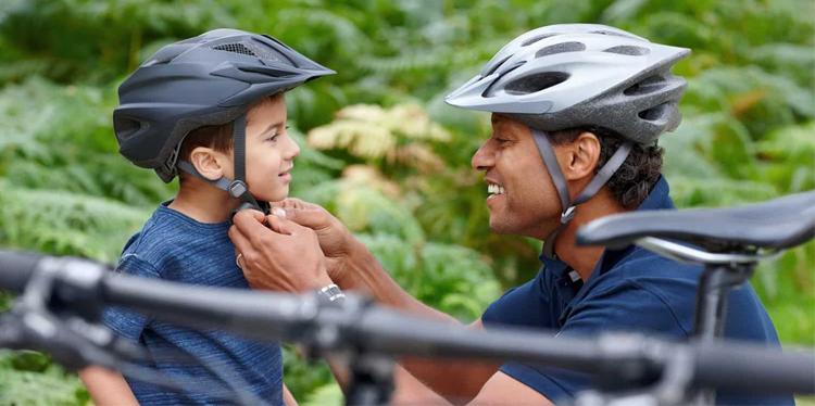 Father in a bike helmet putting helmet on his young son