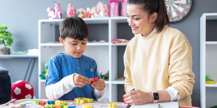 child with adult playing with blocks in a classroom environment