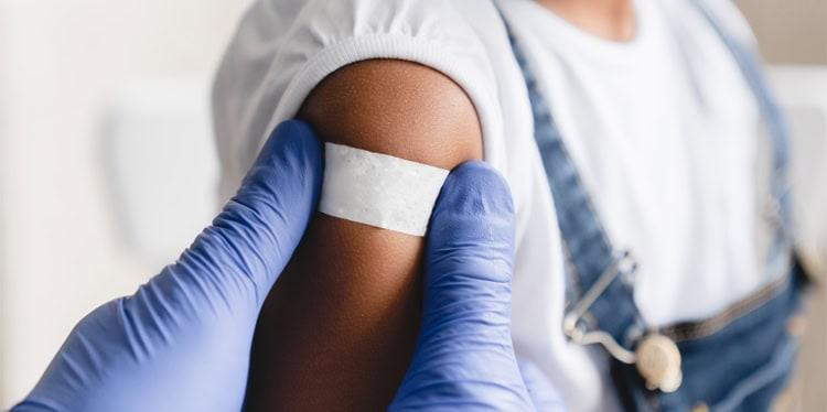 little girl getting vaccinated, bandage over forearm being placed by gloved hands, vaccine, immunity, MMR, travel, infection, measles outbreak