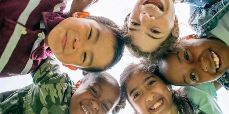 five children looking at the camera in a huddle, celebrating world children’s day, encourage children to participate, provide, protect, participate, books in multiple languages, achieve their health and personal goals