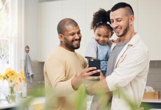 two men holding a child looking at phone