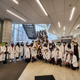 Group photo of students in lab coats posing in an academic building lobby.