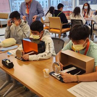 Students using optical and manual tools for a vision and dexterity activity at a table.