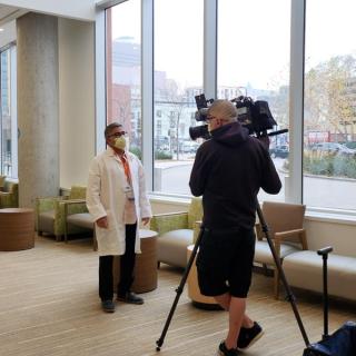 Person in a lab coat being interviewed by a news crew with a video camera.