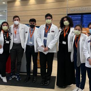 Group of students in lab coats posing for a photo in the lobby of a healthcare facility.