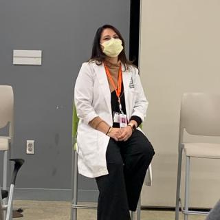 Panelist in a lab coat seated and listening during an educational session.