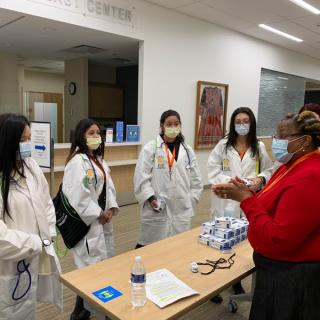 Students receiving materials and information from a staff member at an event table.