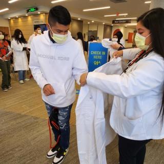 Student assisting another student with putting on a lab coat in a hallway.