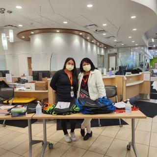 Two women standing behind a check-in table with welcome materials and backpacks.