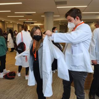 Student helping another student put on a lab coat during orientation.
