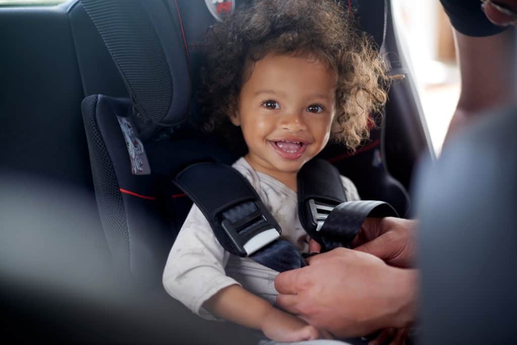 Happy female toddler in backseat car seat getting belted in by adult, passenger safety, child passenger safety, law, car seat, seat belt